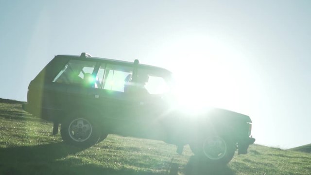 Slow motion footage of vintage 4WD SUV driving down green grassy slope with sunlight shining through windows