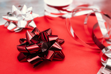 large red foil bow for packaging and decoration on a red and silver background and packing ribbons on the background.