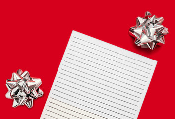 white lined sheet of paper on red background with a silver foil bow