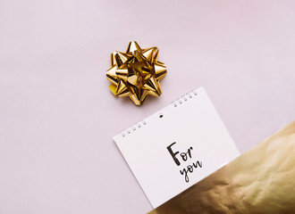 gold bow for decoration and notebook on a spiral with white sheets and black lettering for you on a delicate beige with gold foil background