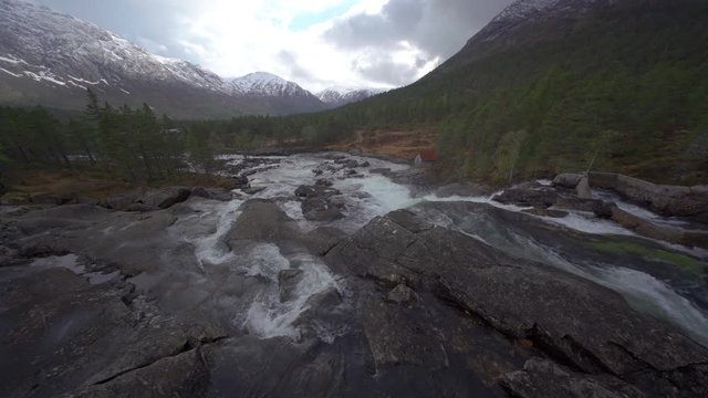 A beautiful view from the Likholefossen bridge. Clear transparent water rushing over the smooth stone riverbed, carrying white foam and whirling. Gray gloomy sky hanging above.