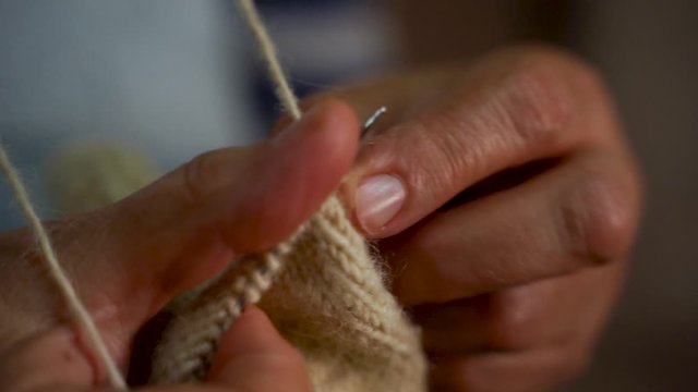 Hands of old woman knitting handmade wool socks with needles at home, slow motion, close up grandma