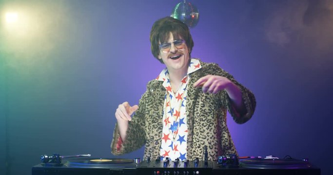 Cheerful Caucasian retro style DJ with mustache in leopard jacket mixing music at party. Smiling man having fun and dancing. Stylish happy model djing on audio equipment. 50s vintage concept