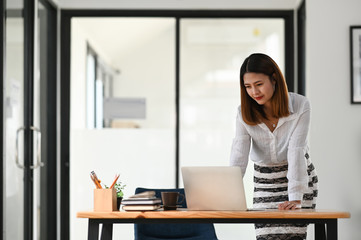 Beautiful woman working as secretary standing and look at her computer laptop over comfortable office as background.