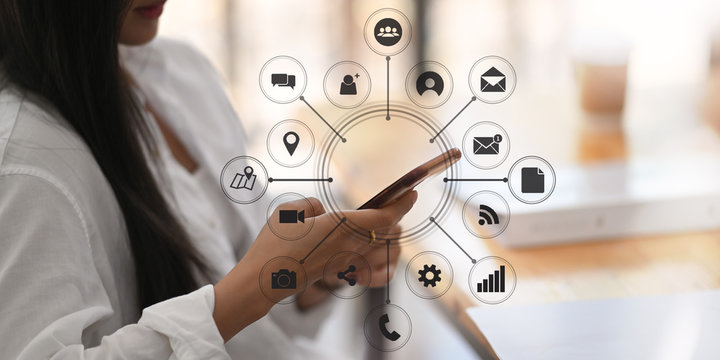 Cropped beautiful woman sitting at comfortable sitting room and using/holding a smartphone with showing virtual icons graphics/ interface on screen.