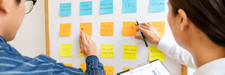 Business people arranging sticky notes commenting and brainstorming on work priorities colleague in a modern co-working space.