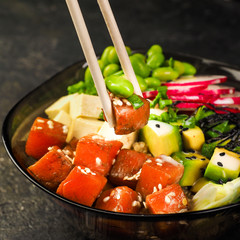 poke bowl on rice and quinoa. Closeup photo of chopsticks and a piece of salmon and tuna. seafood hawaiian cuisine. trendy modern menu dish