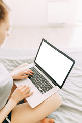 Fototapeta premium The girl works at home on the sofa with a laptop. The girl works from home lying on the bed. Online earnings during the quarantine.