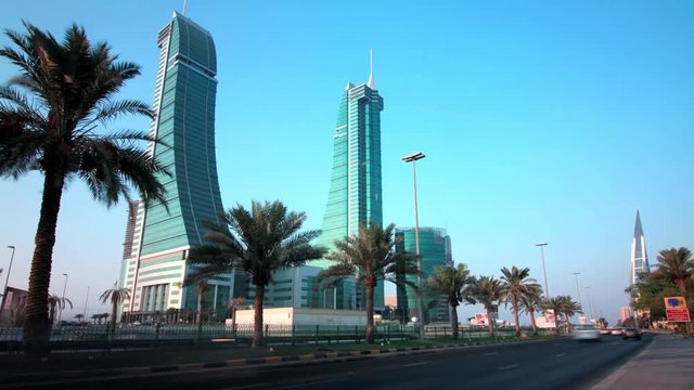Timelapse of the King Faisal Highway in Manama with cars speeding in the foreground and the iconic Bahrain Financial Harbour twin towers in view with palm trees in the median.