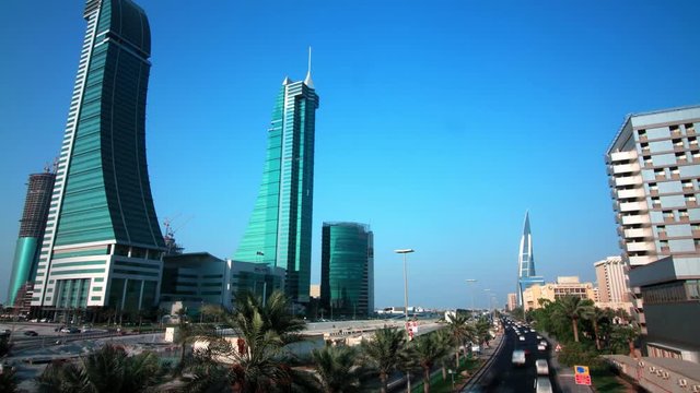 Tilting up moving timelapse of the King Faisal Highway in Manama with cars speeding in the foreground and the iconic Bahrain Financial Harbour twin towers in view with palm trees in the median.