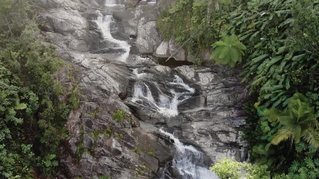 Flying up rocky waterfall with dense forest with cracks and fast flowing water