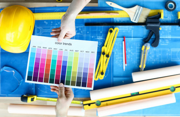 Top view of worker holding paper with colour trends. Colourful palette swatch for designer. Tools and project plan on table. Renovation and construction site concept