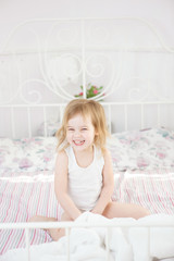Naklejka premium little girl smiling sitting on bed in bedroom.