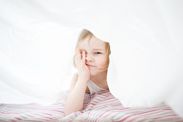 small girl playing under blanket on bed.