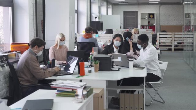 Modern international office, working and communicate in an open space, office workers and managers in medical masks working at computers, protection from the virus, working during the pandemic.