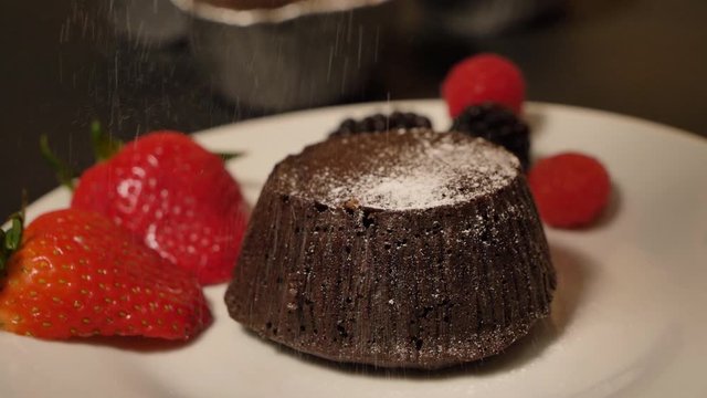 Dessert cook decorates tasty cupcakes white cream topping with cutted strawberry pieces at kitchen