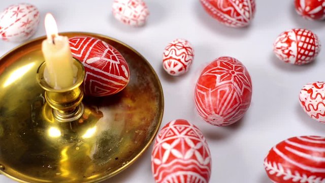 Red easter eggs with folk Ukrainian pattern lay around and on candlestick with burning candle. And man rotate one egg on white background. Ukrainian traditional eggs pisanka and krashanka