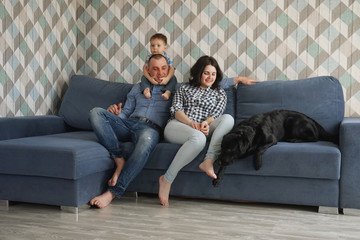 Young family mother, father and son sitting on a blue sofa with a black labrador retriever dog during quarantin. Stay home Self-isolation.