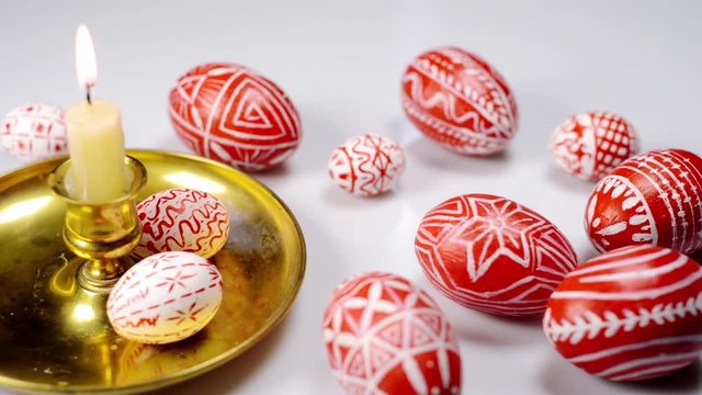 Red easter eggs with folk Ukrainian pattern lay around and on candlestick with burning candle. And man rotate one egg on white background. Ukrainian traditional eggs pisanka and krashanka