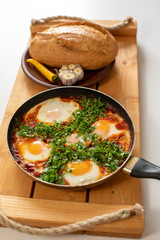 Shakshuka stands on a wooden table. Tasty shakshuka with bread. Top view. Close up.