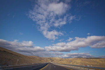 Asphalt road and bright blue sky with fluffy clouds . Empty desert asphalt road from low angle with mountains and clouds on background. road, red desert landscape . Open road with blue clouds .