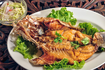 Fried fish with fish sauce and mango salad In a white plate on a wooden table