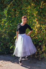 Fototapeta premium Woman ballerina in a white ballet skirt dancing in pointe shoes in autumn park.