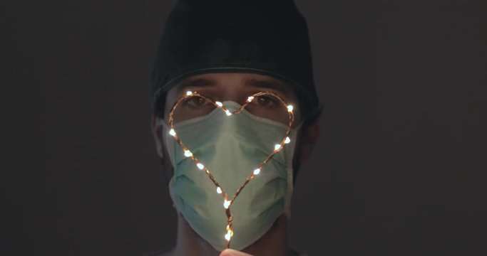 Occhi in primo piano di un medico in prima linea alla lotta al Coronavirus tiene in mano un piccolo simbolo del cuore luminoso per dare speranza alla fine della pandemia Coroanvirus.