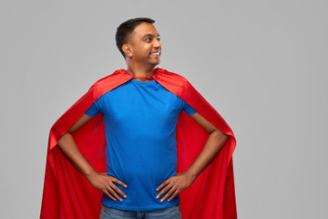 super power and people concept - happy smiling indian man in red superhero cape with arms on hips...