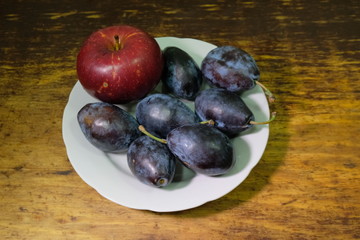 beautiful red apple and plums in a plate on a dark wooden background