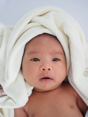 The Asian baby girl just took a shower. She is lying down and let her mother wipe the body dry and clean by using a soft towel to wipe. There is a soft towel on her head.
