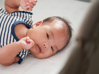 Asain newborn baby girl is wearing new strip cloth awake in a baby cot and smiling.