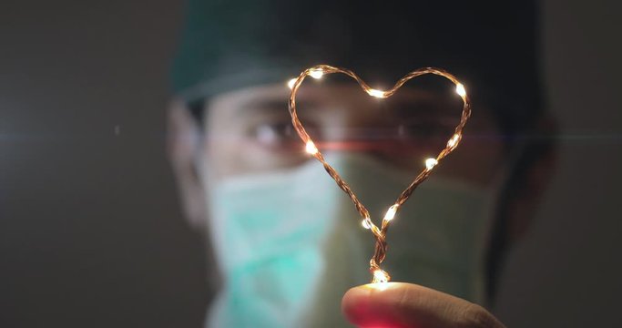 Occhi in primo piano di un medico in prima linea alla lotta al Coronavirus tiene in mano un piccolo simbolo del cuore luminoso per dare speranza alla fine della pandemia Coroanvirus.