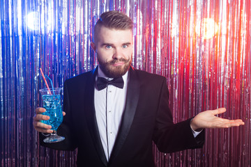 Club party, emotions and holidays concept - Portrait of elegant disappointed handsome man in a expensive suit holds blue cocktail on shiny background.