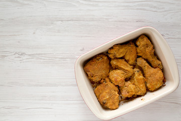 Crispy homemade oven baked fried chicken in a dish on a white wooden background, top view. Flat lay, overhead, from above. Copy space.