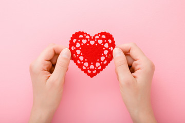 Obraz premium Young woman hands holding red heart shape on light pink table background. Pastel color. Love and happiness concept. Closeup. Point of view shot. Top down view.
