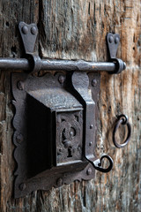 Ancient rusty steel lock bolt with a key hole installed on an old wooden door from medieval age