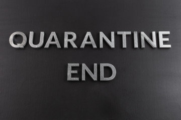 the words quarantine end laid with silver metal letters on matte back flat surface directly above...