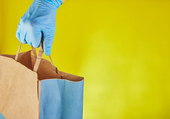 Delivery man employer in blue gloves hold craft paper bag with food, isolated on yellow studio background. Service quarantine pandemic coronavirus virus concept 2019-ncov. copy space.