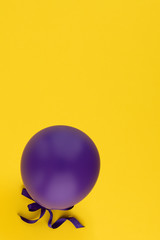 Violet balloon isolated on a yellow background. Vibrant Purple balloon in the bottom corner. Copy space. Party decoration for celebrations and birthday. 