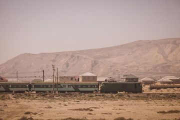 Side view of electric passenger train with green locomotive and passenger coaches in the plains or deserts of Azerbaijan, close to Baku.