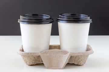 Two white disposable cups with lids in a cardboard tray