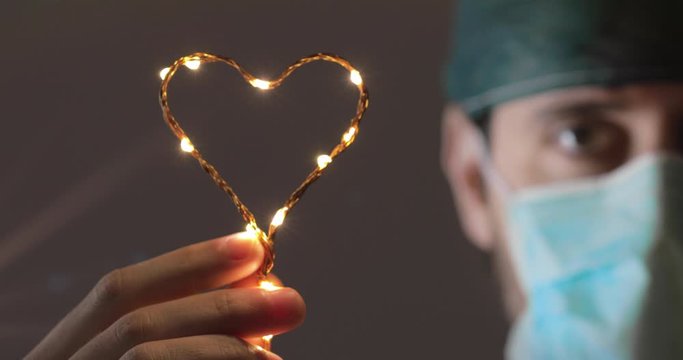 Primo piano di un giovane medico con mascherina che tiene in mano un cuore per ricordare i suoi colleghi vittime del Coronavirus covid-19 in Italia