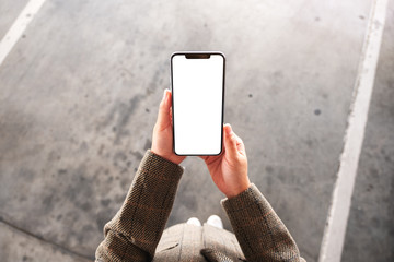 Top view mockup image of a woman holding mobile phone with blank white screen on the street