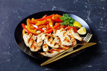 Grilled chicken breast pieces on a black plate