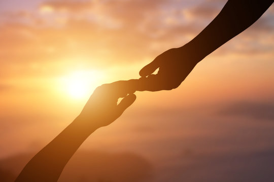 Silhouette of giving a helping hand, hope and support each other over sunset background.