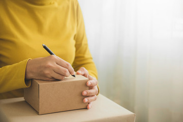 Young woman working and writing customer address on packaging parcel box for send order to customer...