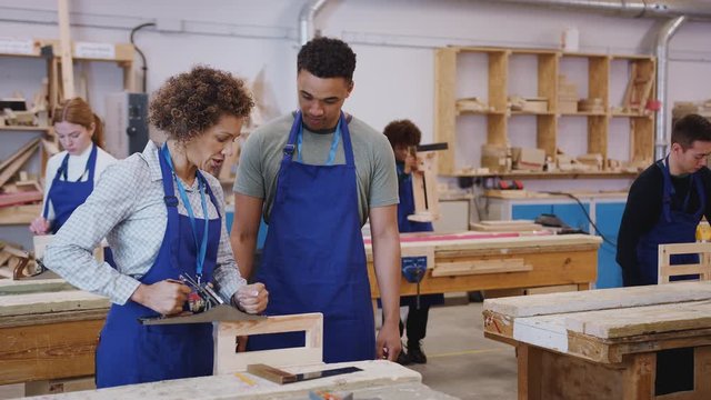 Dolly shot of female tutor with carpentry student in workshop studying for apprenticeship at college using wood plane - shot in slow motion