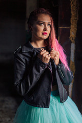 Naklejka premium Portrait of a young girl with pink hair standing next to the old rusty door inside of collapsed building surrounded by ruins