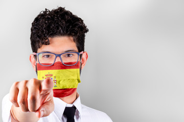 Man in mask with Spain flag pointing at you. Stay at home concept.